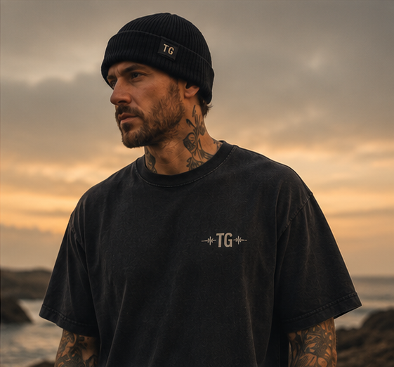 Portrait of a bearded man in a black beanie and Tinnitus Gang tee, calm coastal light