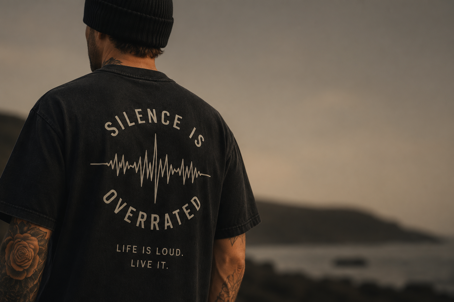 Back view of a man in a black tee printed with “Silence Is Overrated” on a coastal shore